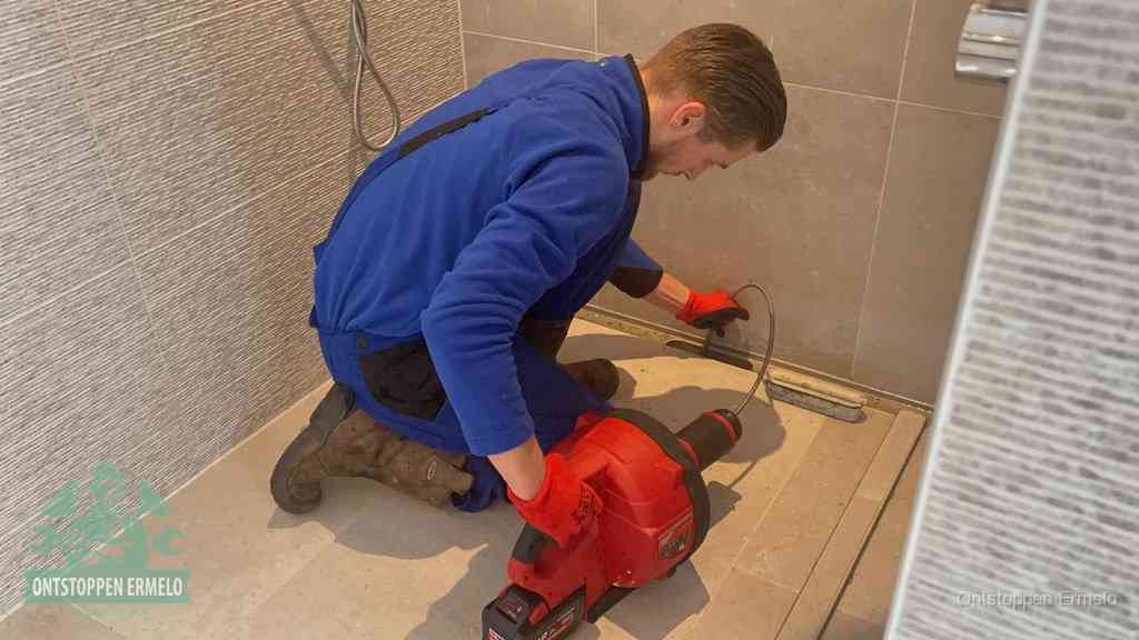 Een monteur ontstopt een langwerpige douchegoot met een elektrische veer, een doucheputje verstopt door haren en zeep in Ermelo